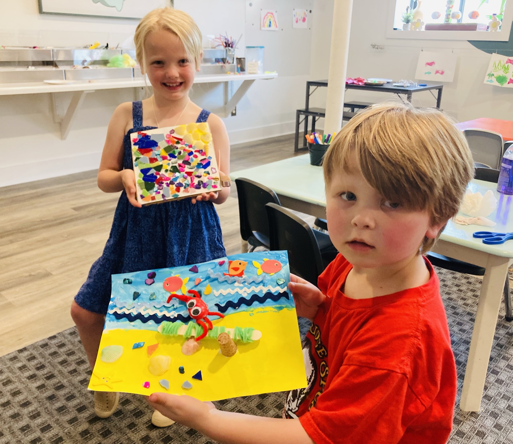 Two children showing colorful mixed-media artwork at Little Beasties