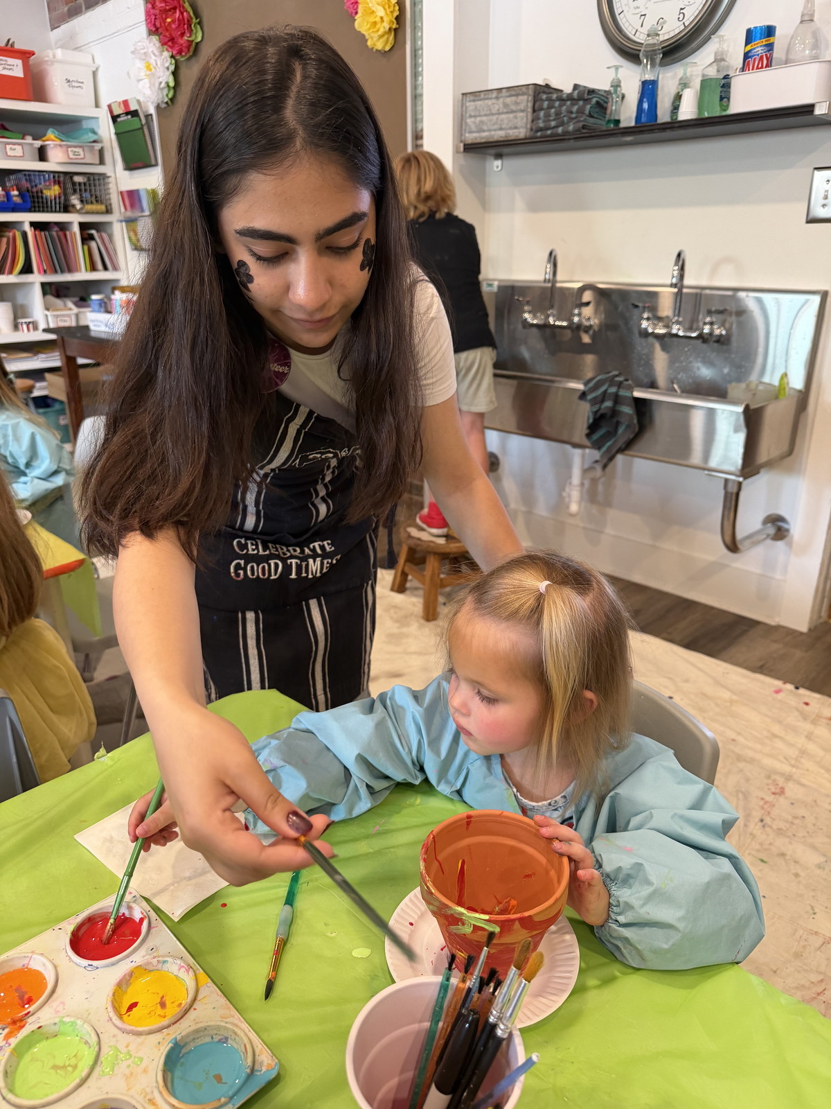 Art instructor helping a child paint at a studio table