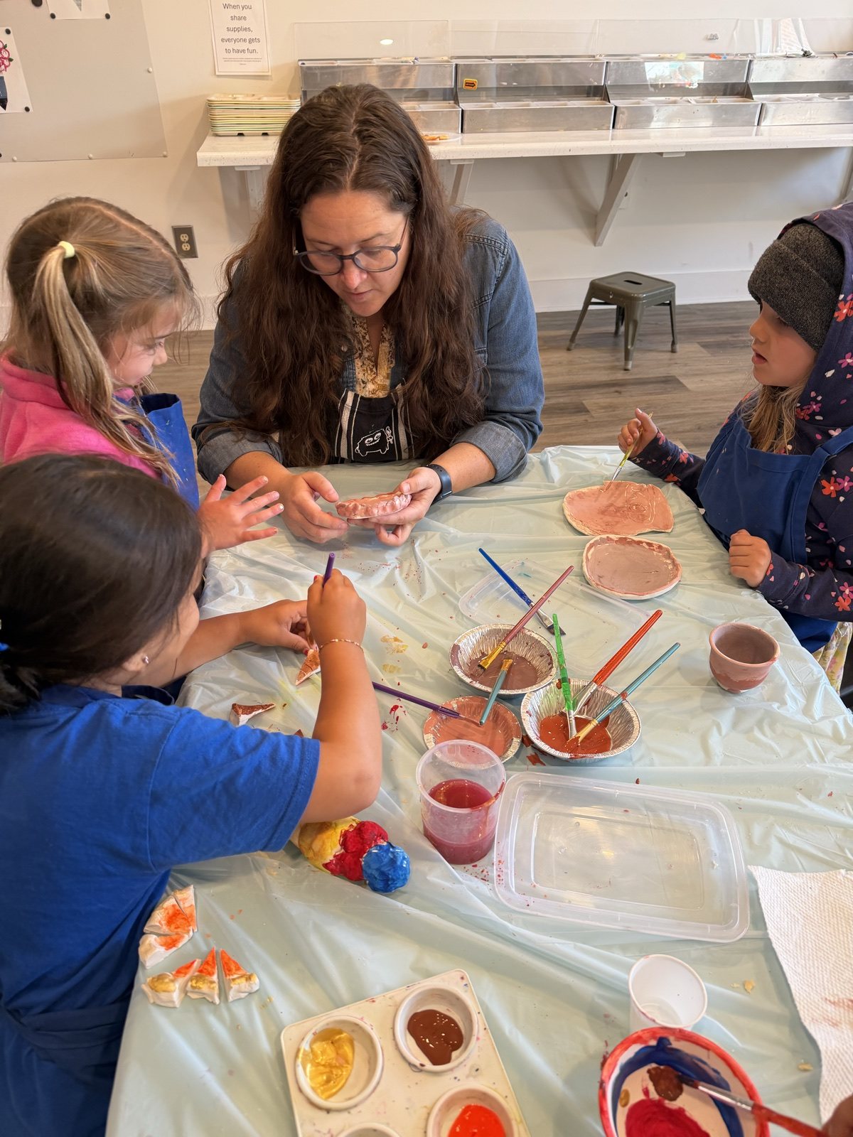 Art instructor guiding children through a clay project at the studio table