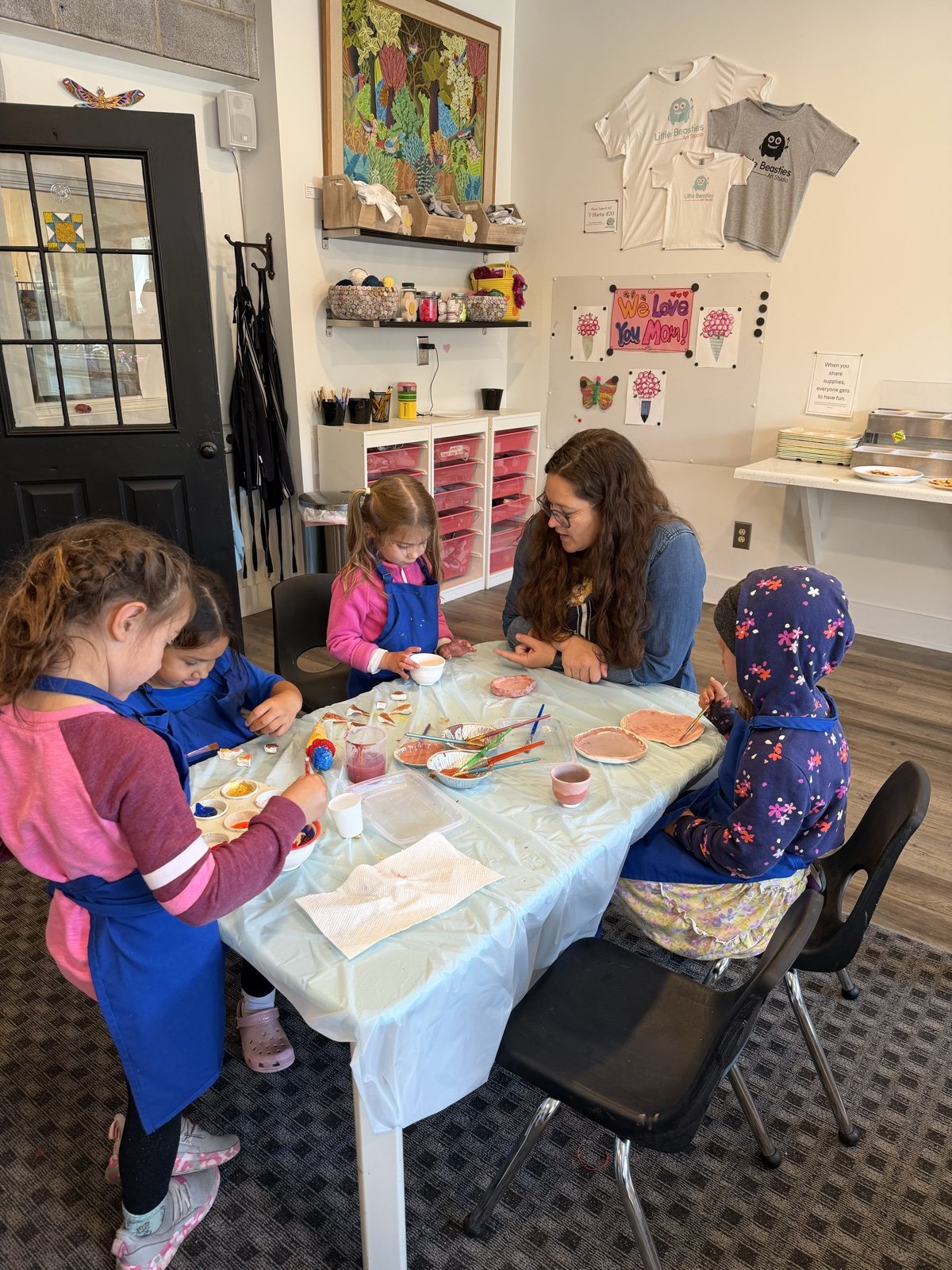 Art instructor helping four children create clay projects around a studio table