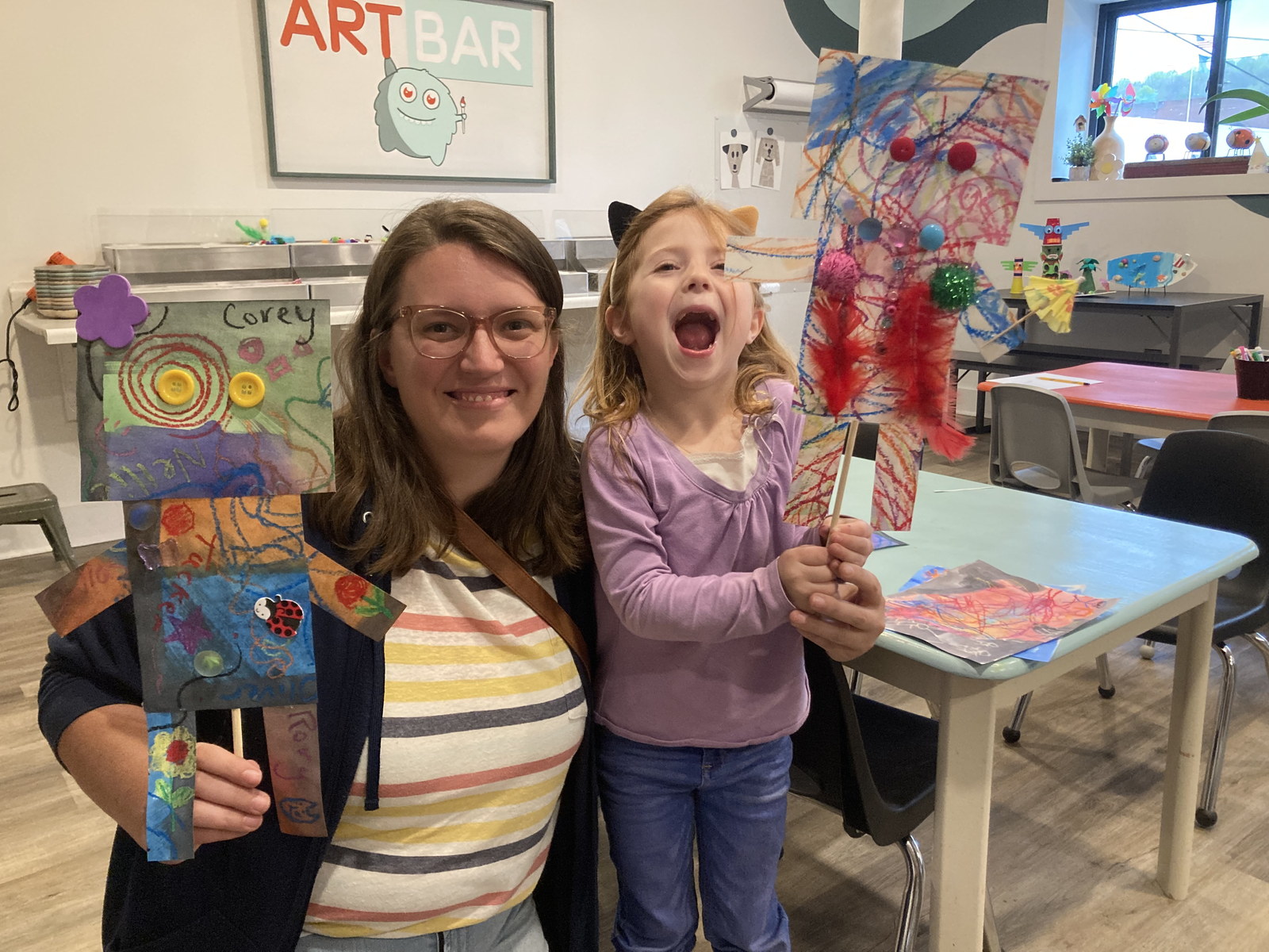 A mother and daughter proudly holding up their colorful art projects together