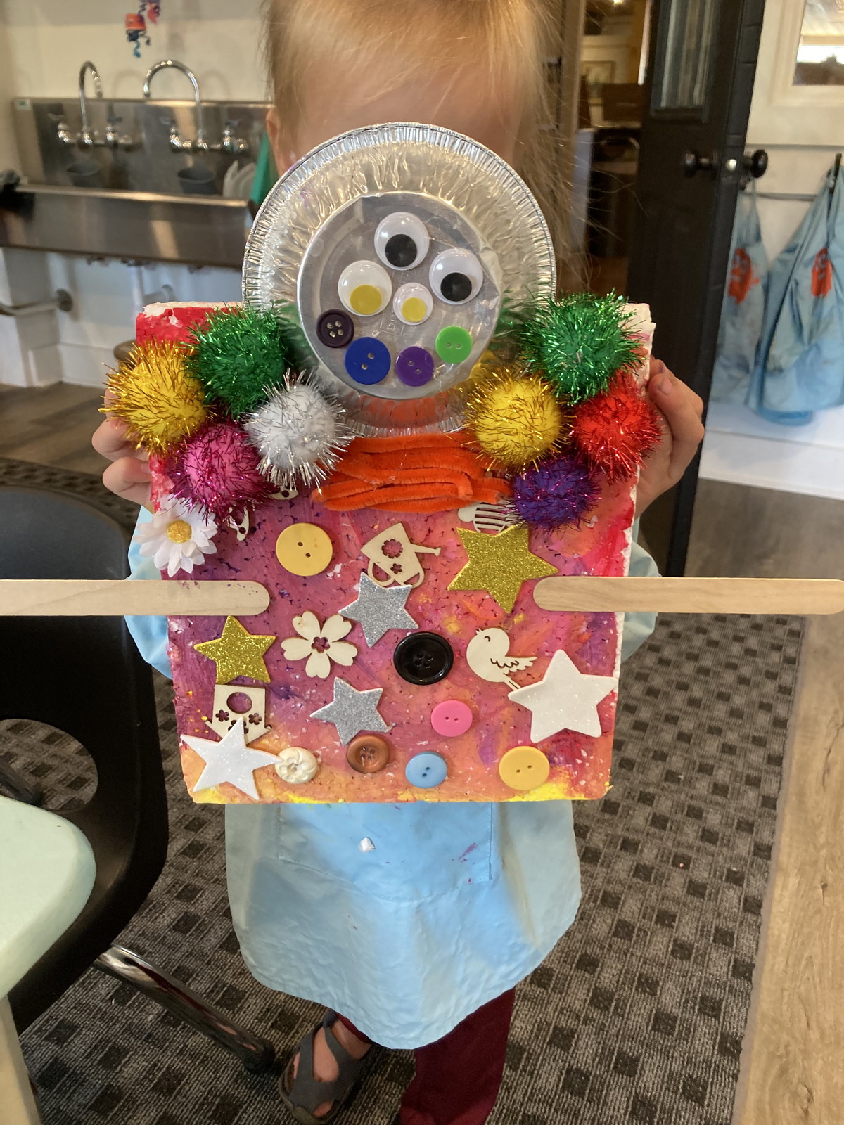 Child holding a colorful mixed-media sculpture
