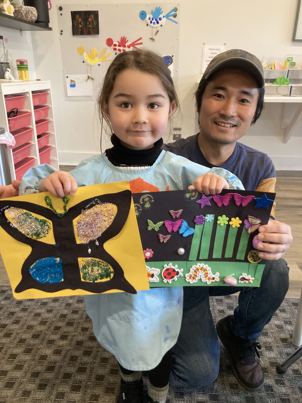 Two children holding butterfly and flower collage artwork