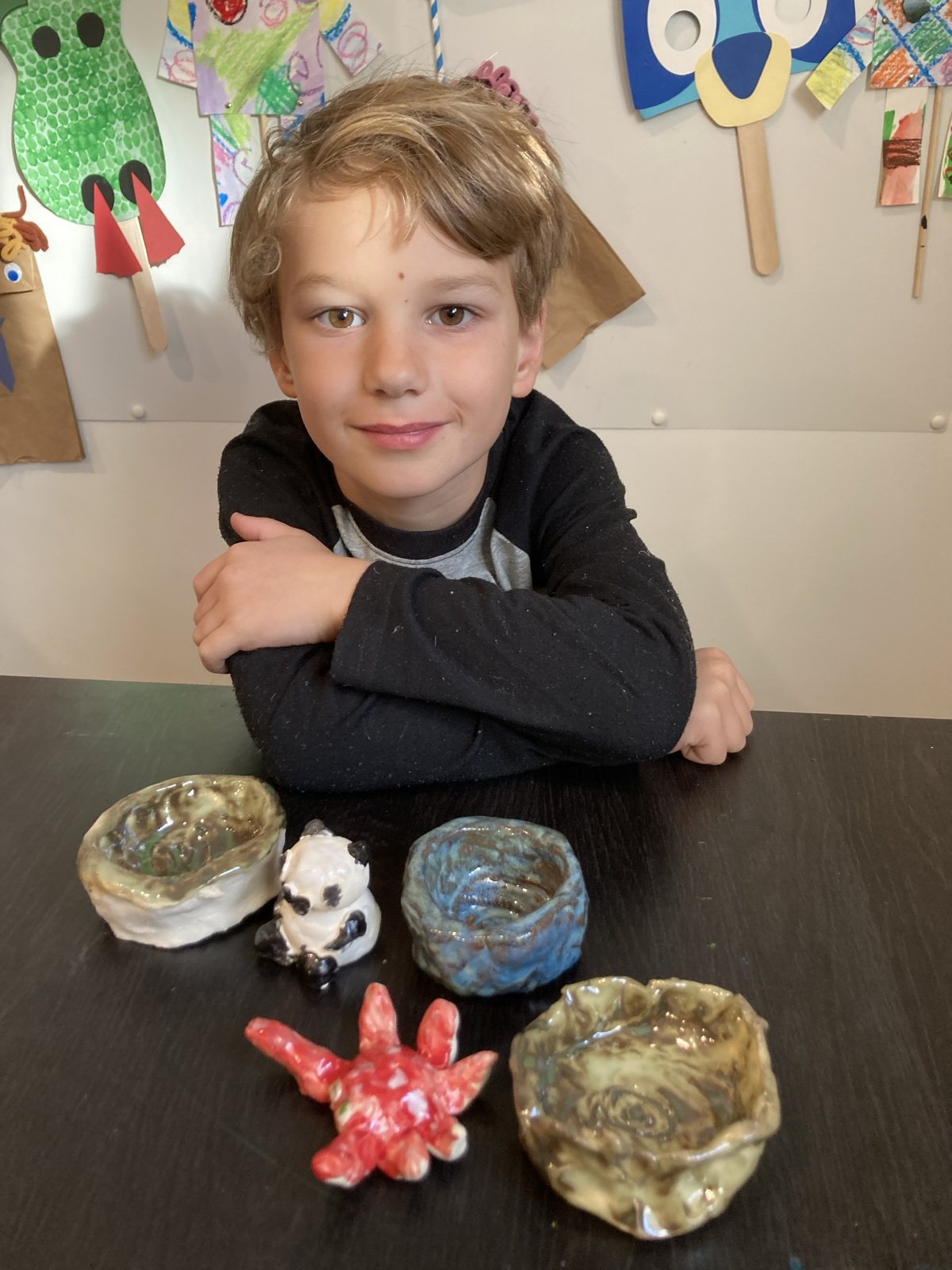 Child displaying handmade clay bowls and small sculptures