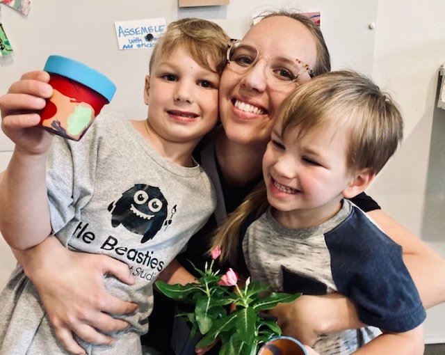 A smiling mother and two young artists showing a painted flowerpot