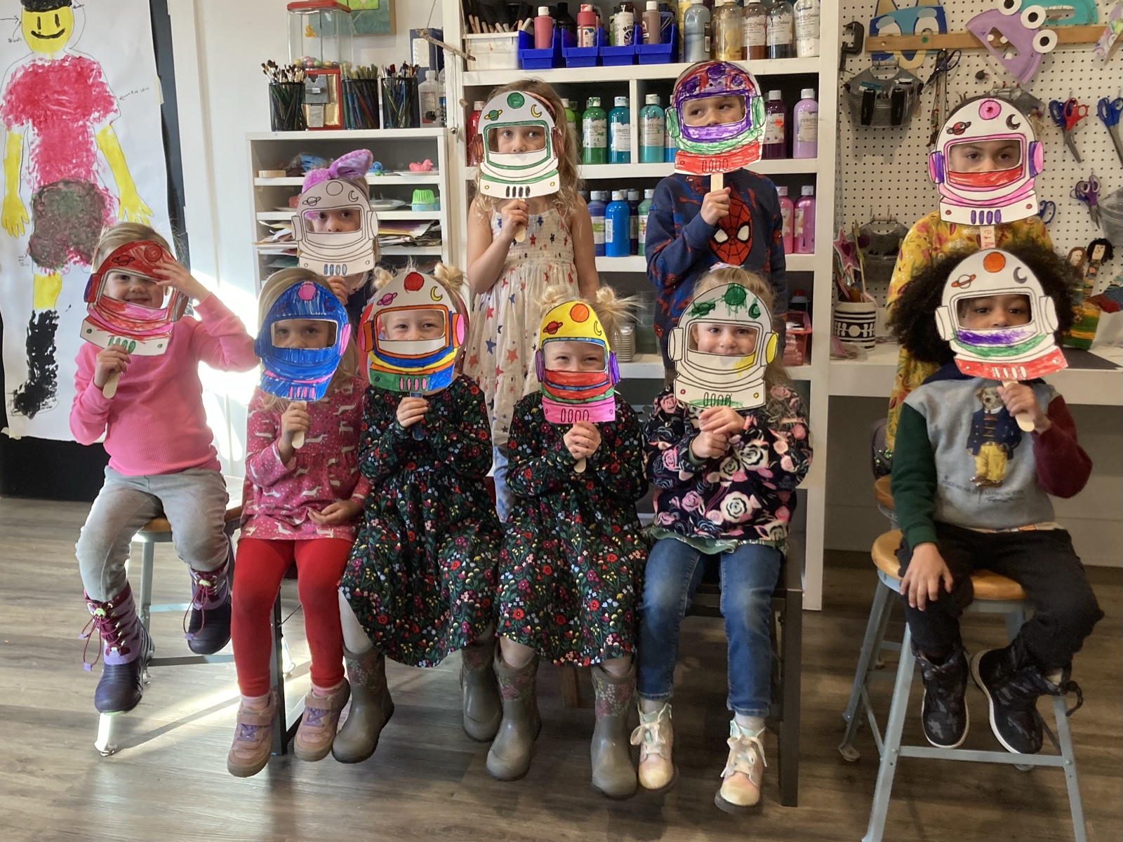 Young artists holding their colorful astronaut-mask projects in the studio