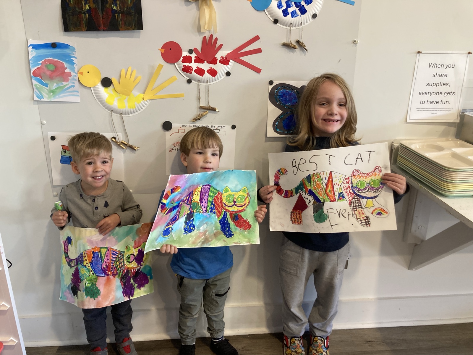 Three young artists showing colorful cat artwork at Little Beasties